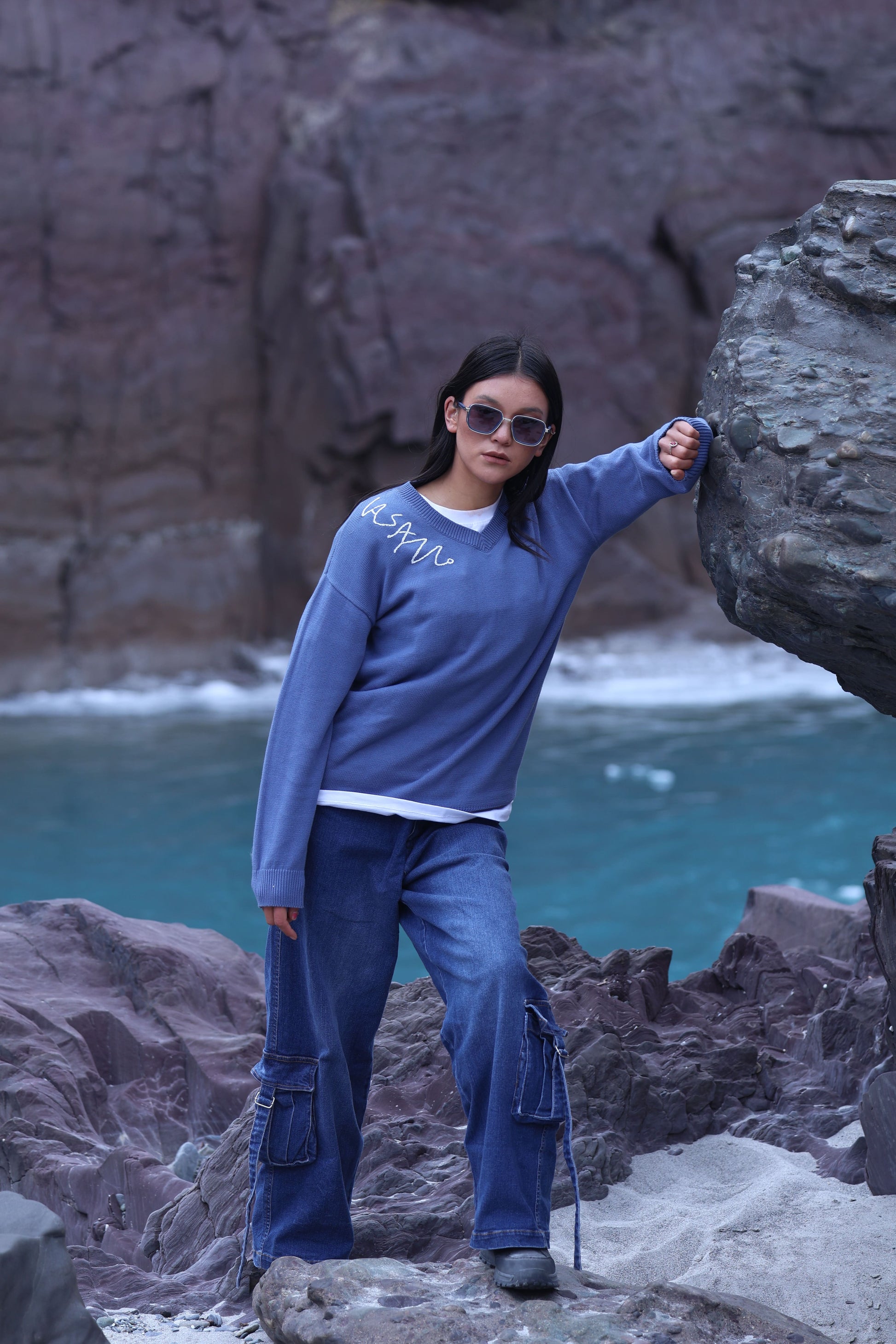 Person in blue outfit standing on rocky terrain with ocean and cliffs in the background