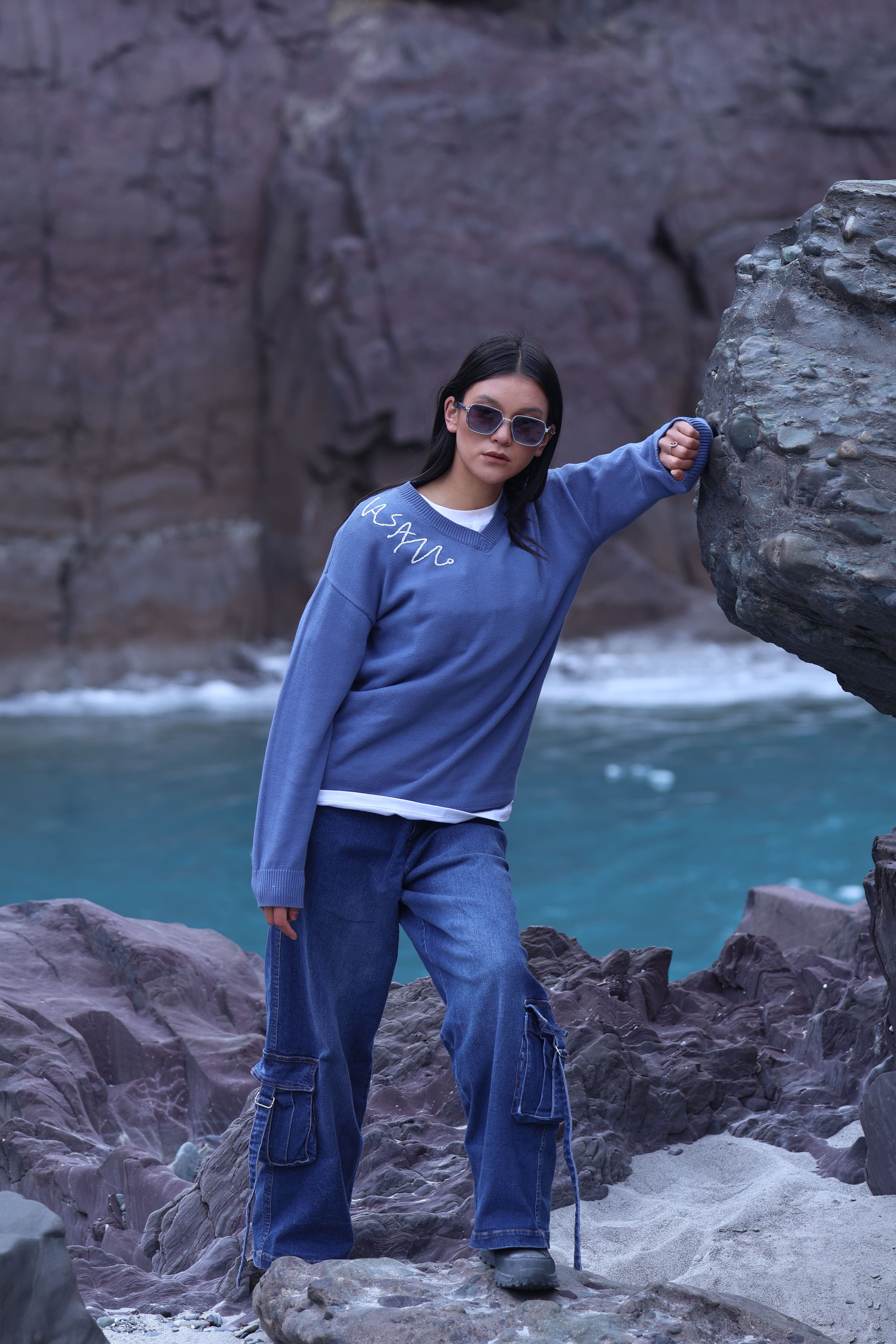 Person in blue outfit standing on rocky terrain with ocean and cliffs in the background